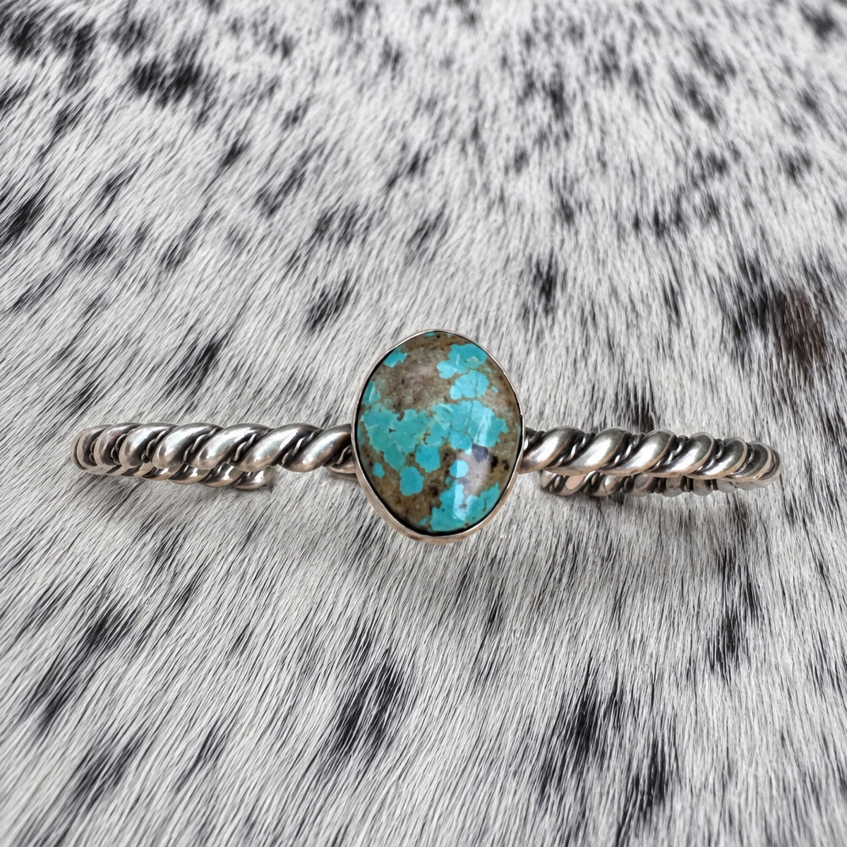 Elaine Tahe Navajo Artist Turquoise and Silver Twisted Wire Bracelet on gray-and-white cowhide