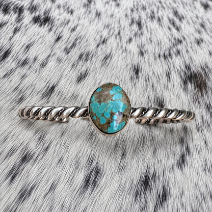 Elaine Tahe Navajo Artist Turquoise and Silver Twisted Wire Bracelet on gray-and-white cowhide