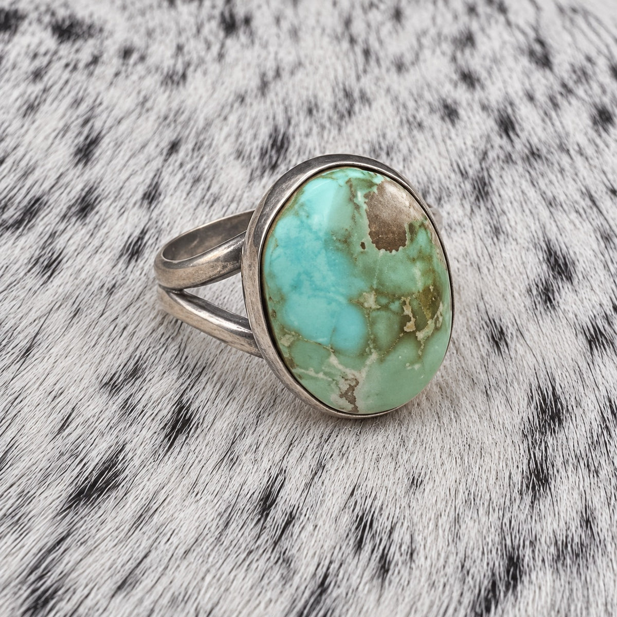 Sonoran Turquoise Ring by Susan Cooke — angle view on gray-and-white cowhide